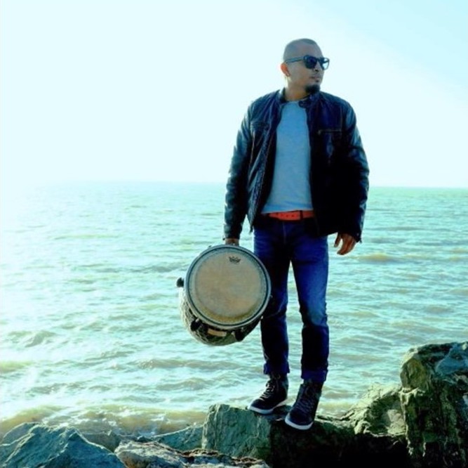 Photo of musician Silvestre Martinez standing on rocks in front of water