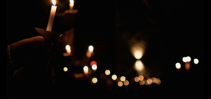 Photo of a person holding a candle that was lit by others. Light shining in the darkness.