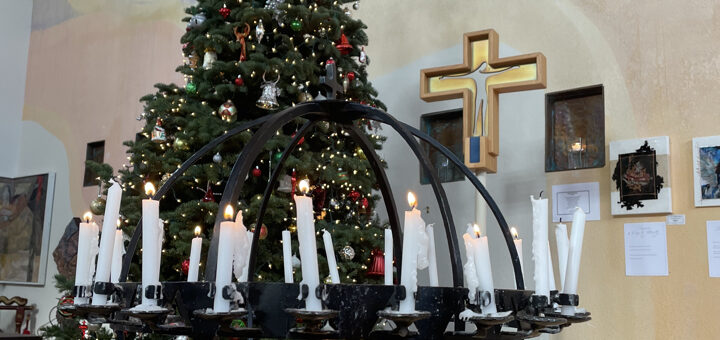 A photo of the Peace Light Globe with candles lit during Worship, with the Christmas Tree and Processional Cross.