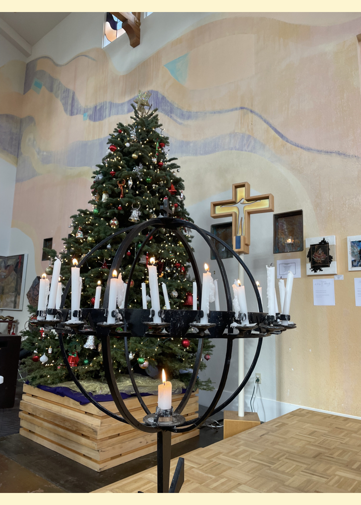 A photo of the Peace Light Globe with candles lit during Worship, with the Christmas Tree and Processional Cross.