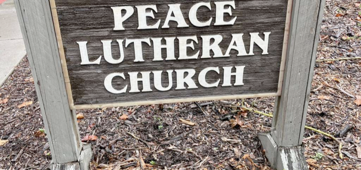 The sign reading "Peace Lutheran Church" with a cross and palm branch at the entrance to the Church parking lot.