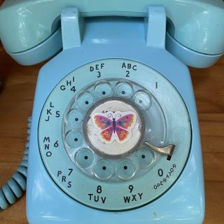 Close up of the Peace Wind Phone, a bright blue disconnected rotatory phone with a butterfly sticker at the center.