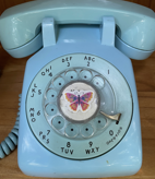 Close up of the Peace Wind Phone, a bright blue disconnected rotatory phone with a butterfly sticker at the center.